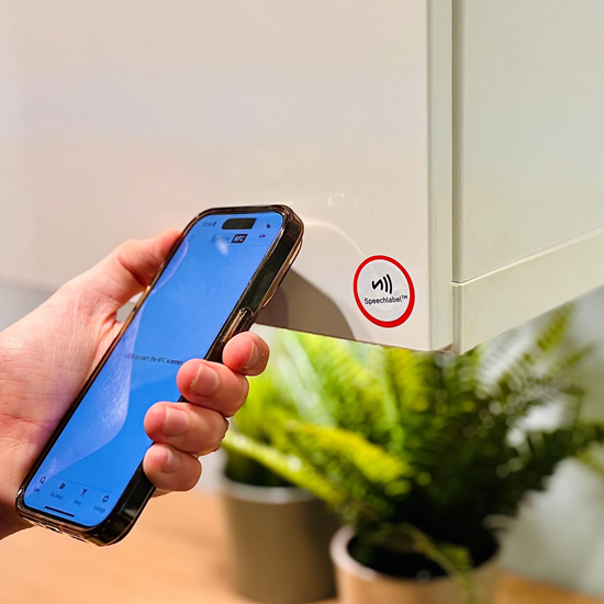 Zdjęcie przedstawia osobę używającą smartfona do identyfikacji szafki kuchennej poprzez przyłożenie telefonu do etykiety NFC marki Hable One